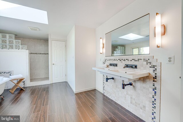 bathroom with wood finish floors, a soaking tub, a skylight, walk in shower, and tasteful backsplash