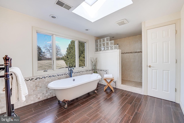 bathroom featuring visible vents, a walk in shower, tile walls, a skylight, and a soaking tub