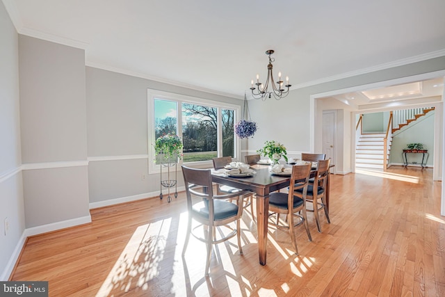 dining area featuring a notable chandelier, crown molding, light wood finished floors, baseboards, and stairs