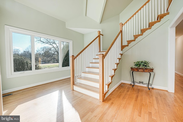 stairs with visible vents, vaulted ceiling with beams, baseboards, and wood finished floors