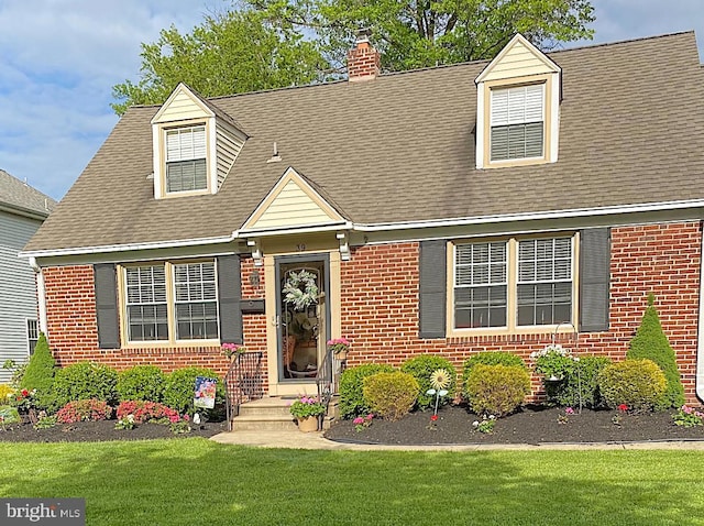 cape cod home with brick siding, a front lawn, a chimney, and a shingled roof