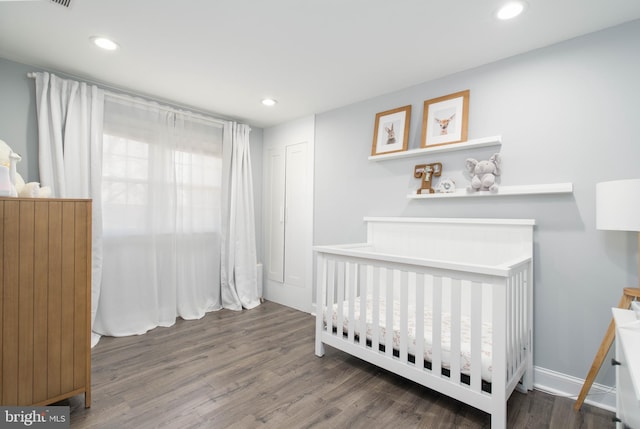 bedroom featuring recessed lighting, a crib, baseboards, and wood finished floors