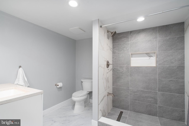 bathroom with toilet, marble finish floor, a tile shower, baseboards, and vanity