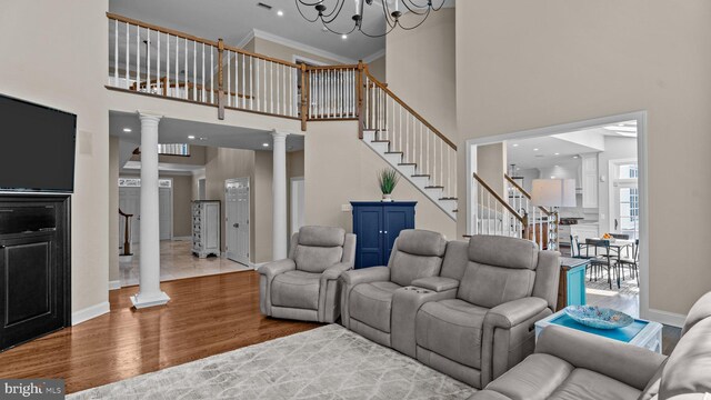 living room with decorative columns, wood finished floors, stairs, and ornamental molding