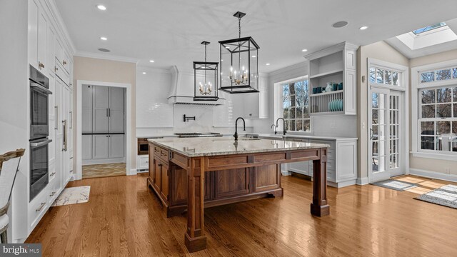 kitchen featuring white cabinets, wood finished floors, stainless steel double oven, and a sink