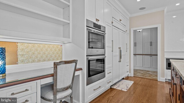 kitchen featuring light wood-type flooring, built in desk, double oven, white cabinets, and crown molding