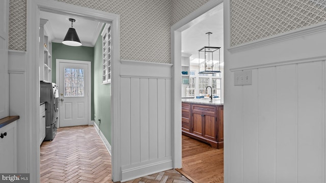 hall featuring a wainscoted wall, wallpapered walls, brick floor, a sink, and washer and dryer