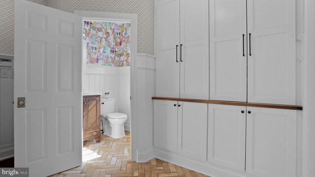 bathroom featuring a wainscoted wall, toilet, and wallpapered walls