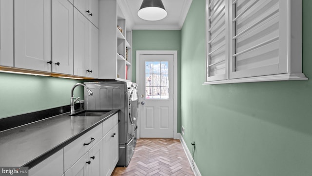 clothes washing area with ornamental molding, a sink, washing machine and dryer, cabinet space, and baseboards