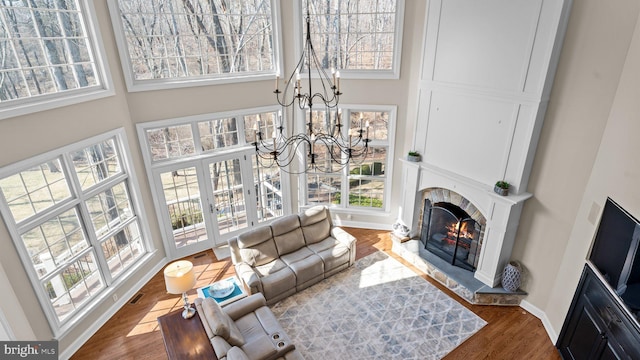 living room featuring baseboards, a warm lit fireplace, a high ceiling, an inviting chandelier, and wood finished floors