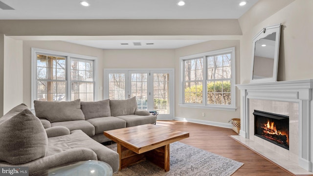 living area featuring a tiled fireplace, wood finished floors, visible vents, and a healthy amount of sunlight