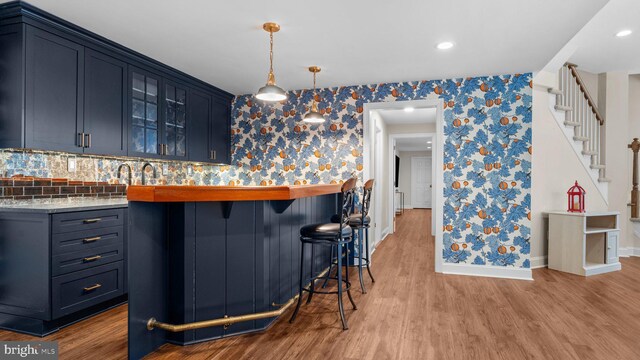 bar featuring light wood-type flooring, pendant lighting, wallpapered walls, baseboards, and stairs