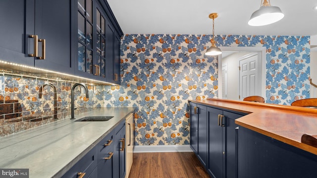 kitchen featuring pendant lighting, a sink, dark wood finished floors, wallpapered walls, and baseboards