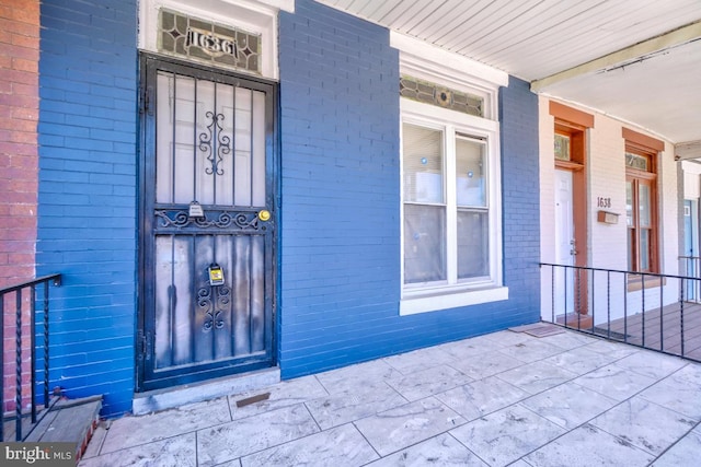 doorway to property with a porch and brick siding