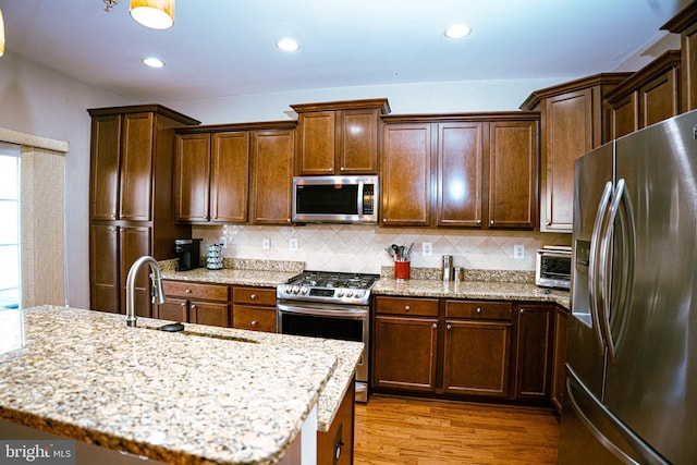 kitchen with stainless steel appliances, wood finished floors, backsplash, a sink, and light stone countertops