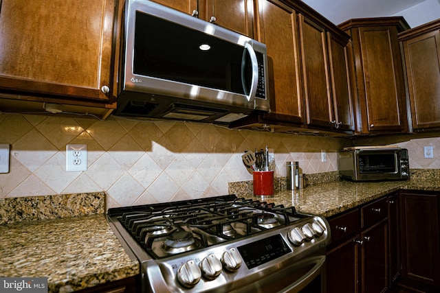 kitchen featuring stainless steel appliances, dark stone countertops, a toaster, and decorative backsplash