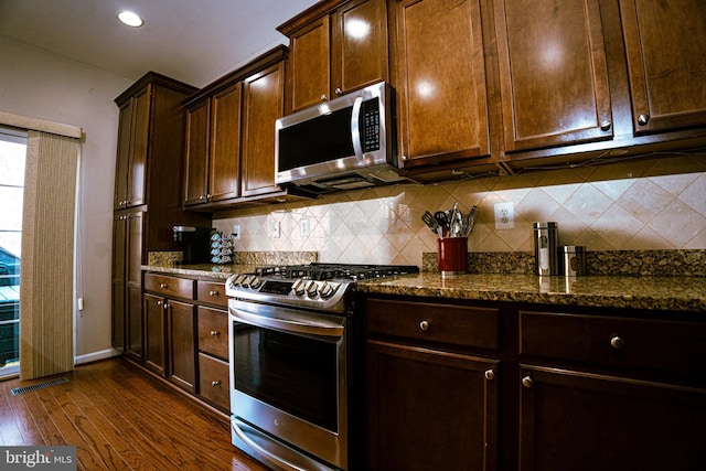 kitchen with stainless steel appliances, dark wood-style flooring, visible vents, backsplash, and dark stone counters