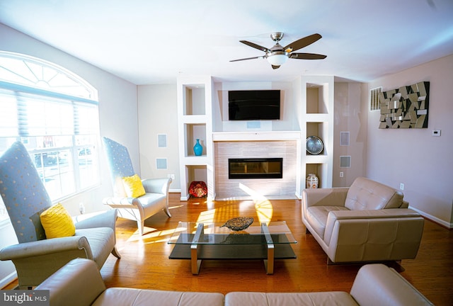 living area with baseboards, a ceiling fan, wood finished floors, and a tile fireplace