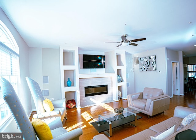 living room featuring a ceiling fan, a tiled fireplace, and wood finished floors