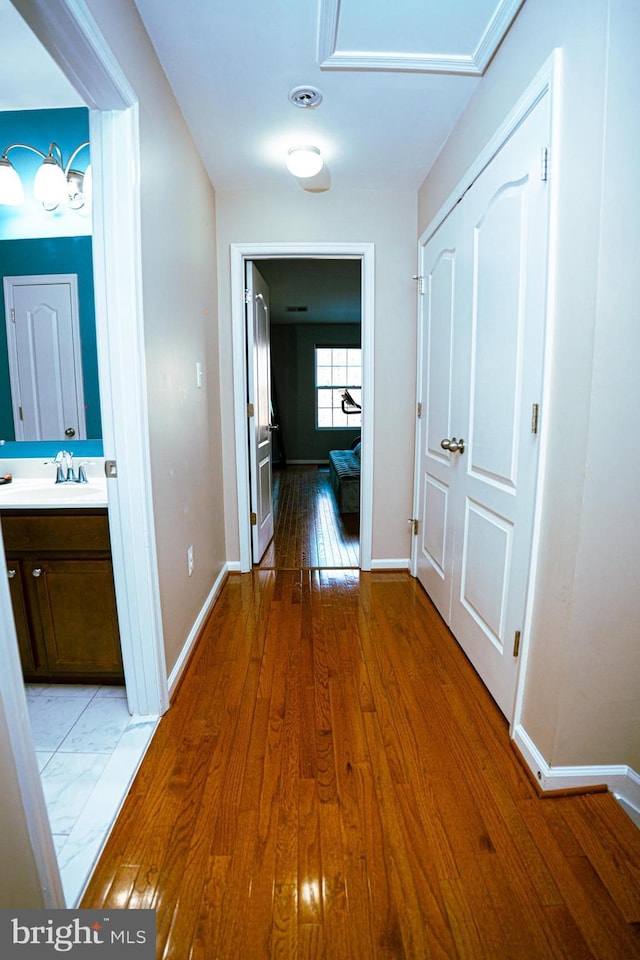 hallway featuring light wood-style floors, a sink, and baseboards