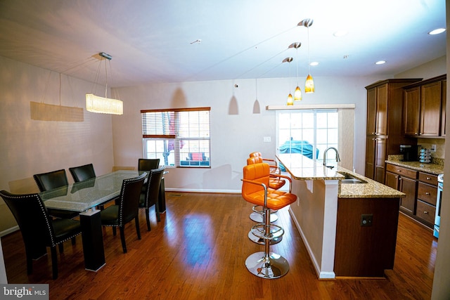 kitchen featuring a center island with sink, baseboards, dark wood-style floors, light stone counters, and a sink