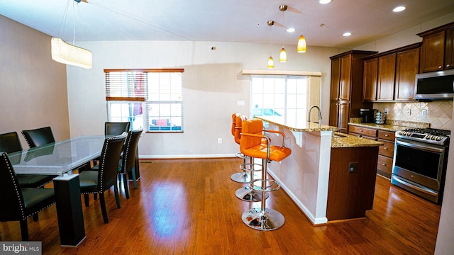 kitchen featuring dark wood-style flooring, decorative backsplash, appliances with stainless steel finishes, a kitchen island with sink, and light stone countertops