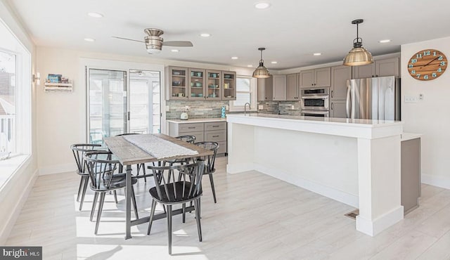 kitchen with stainless steel appliances, gray cabinets, light countertops, backsplash, and glass insert cabinets