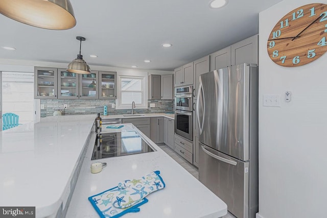 kitchen with a sink, light countertops, stainless steel appliances, gray cabinetry, and backsplash