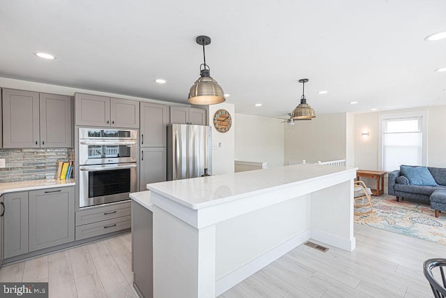 kitchen with appliances with stainless steel finishes, a center island, gray cabinets, and backsplash