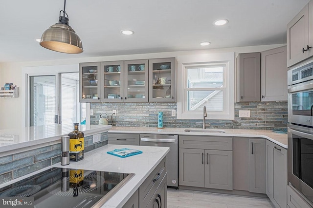 kitchen featuring decorative backsplash, stainless steel appliances, a sink, and gray cabinetry