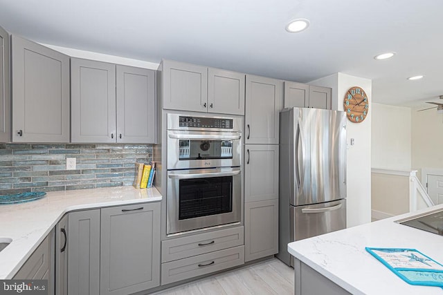 kitchen with appliances with stainless steel finishes, backsplash, gray cabinets, and recessed lighting