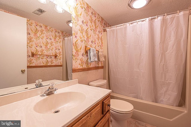 full bath with a wainscoted wall, a textured ceiling, visible vents, and wallpapered walls