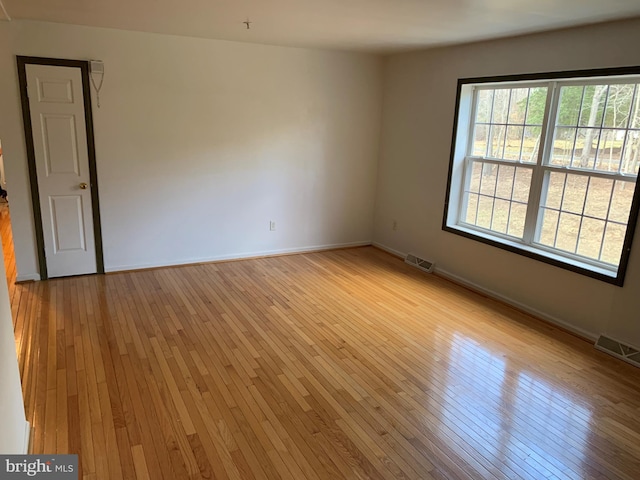 empty room with light wood-type flooring, visible vents, and baseboards