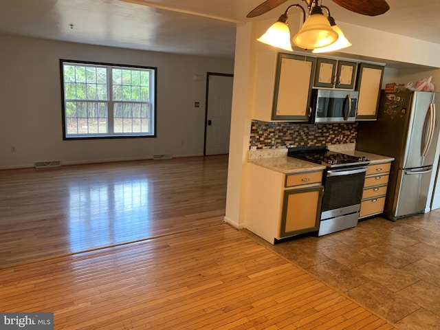 kitchen with stainless steel appliances, light countertops, visible vents, light wood-style flooring, and backsplash