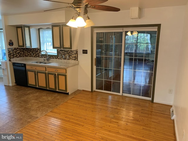 kitchen with black dishwasher, light countertops, backsplash, a sink, and hardwood / wood-style floors