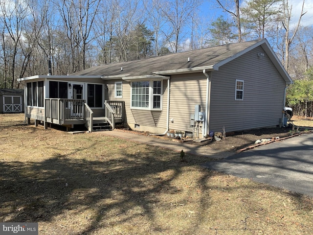 back of house featuring an outbuilding, aphalt driveway, a sunroom, crawl space, and a storage unit