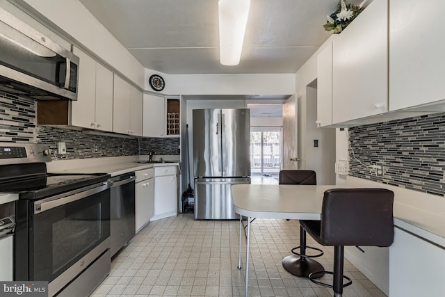 kitchen with a kitchen breakfast bar, appliances with stainless steel finishes, white cabinets, light countertops, and decorative backsplash