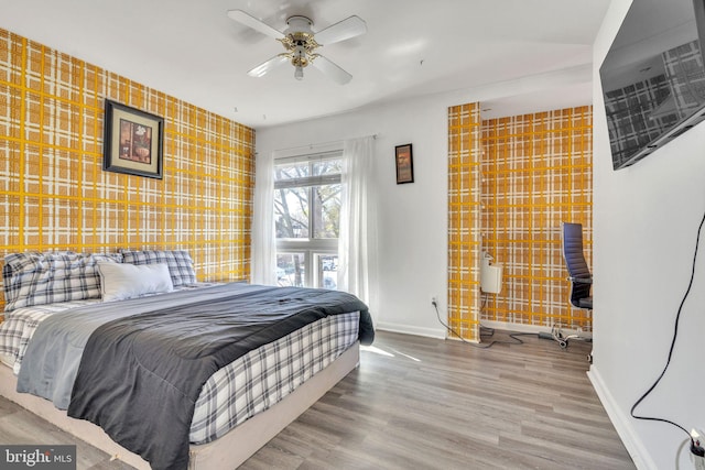 bedroom featuring baseboards, wood finished floors, an accent wall, and wallpapered walls