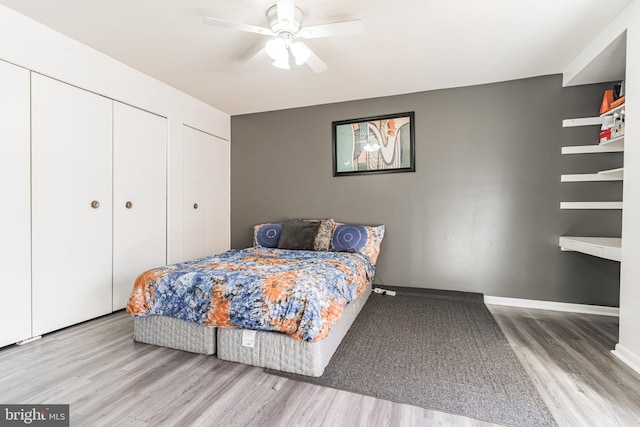 bedroom with baseboards, two closets, a ceiling fan, and wood finished floors