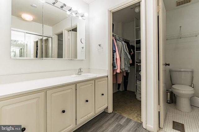 bathroom featuring visible vents, toilet, vanity, and a walk in closet