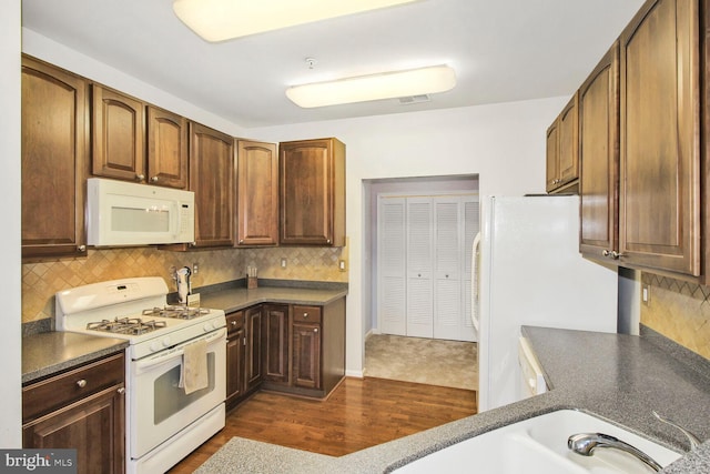 kitchen featuring dark countertops, decorative backsplash, white appliances, and dark wood-style floors