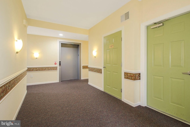 corridor with visible vents, elevator, wainscoting, and dark carpet