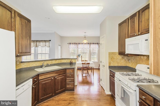 kitchen with dark countertops, tasteful backsplash, light wood-style floors, white appliances, and a sink