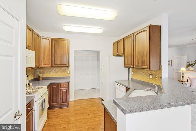 kitchen with tasteful backsplash, light wood-style flooring, a peninsula, white appliances, and a sink