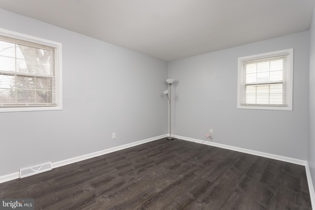 unfurnished room with dark wood-type flooring, visible vents, and baseboards