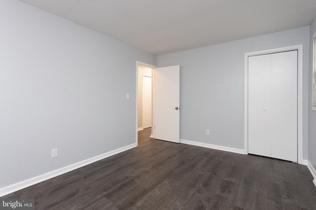 unfurnished bedroom featuring a closet, dark wood-style flooring, and baseboards