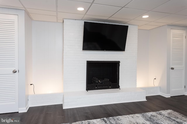 details with a drop ceiling, a brick fireplace, wood finished floors, and baseboards