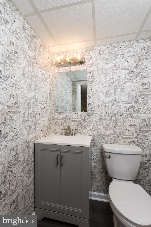 half bathroom with toilet, wallpapered walls, and vanity