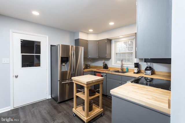 kitchen featuring appliances with stainless steel finishes, dark wood-style flooring, gray cabinets, wooden counters, and a sink