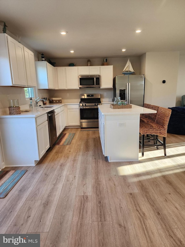 kitchen featuring a center island, light countertops, appliances with stainless steel finishes, white cabinetry, and light wood-type flooring